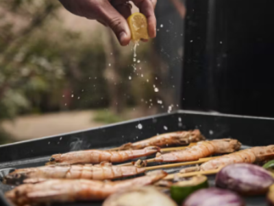 Lemon being squeezed over prawn on a BBQ